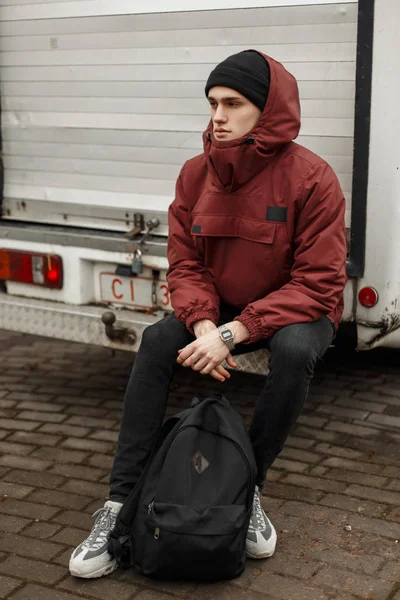 Trendy stijlvolle jonge man in een rood jasje met een kap in een b — Stockfoto