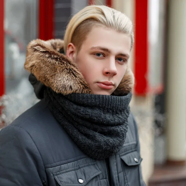 Portrait d'hiver d'un jeune homme avec une coiffure élégante dans une veste d'hiver à la mode et une écharpe dans la rue — Photo