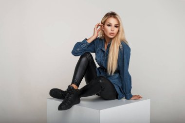 Genç ve güzel Amerikalı manken kadın moda kot gömlek şık ayakkabı ile stüdyoda oturur