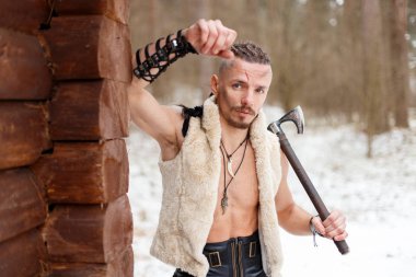 Viking yün bir yelek ormandaki bir ahşap evin yakınındaki bir balta ile
