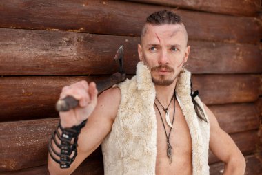 Viking bir saç modeli ile bir yara izi ile cilt standları bir ahşap duvar yakınındaki bir yelek bir balta hold