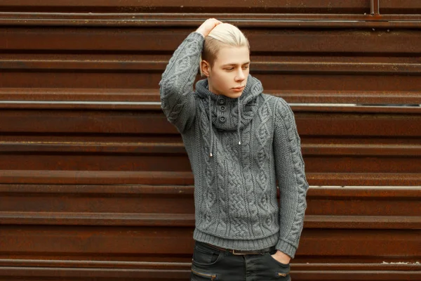 Bello giovane uomo in maglia maglione posa vicino muro di metallo — Foto Stock