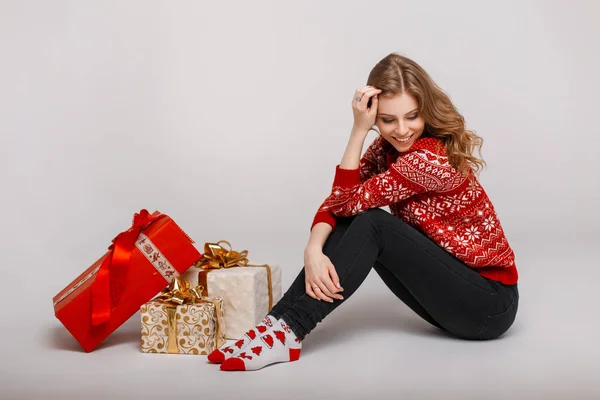 Hermosa joven feliz mujer en un suéter vintage se sienta cerca de regalos sobre un fondo gris —  Fotos de Stock