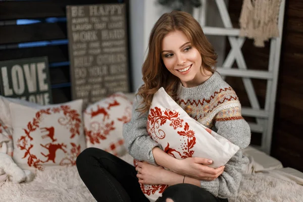 Jeune femme à la mode dans un pull tricoté élégant avec un oreiller assis sur le lit — Photo