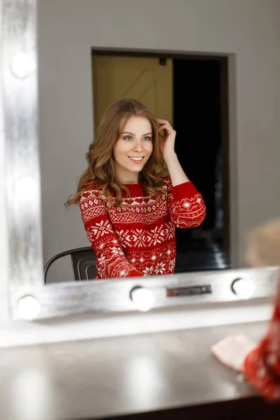 Giovane bella donna in un maglione rosso alla moda guarda allo specchio — Foto Stock