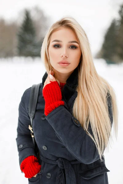 Bastante joven modelo de chica con estilo en un elegante abrigo con un bolso en un día nevado de invierno en el parque —  Fotos de Stock