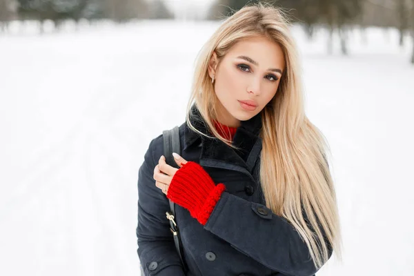 Belle jeune femme blonde en manteau de mode avec pull rouge marchant à l'extérieur sur fond neigeux — Photo