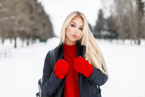 Mujer modelo bastante joven en un elegante abrigo de invierno con un suéter de punto de moda roja al aire libre en un día de invierno nevado —  Fotos de Stock