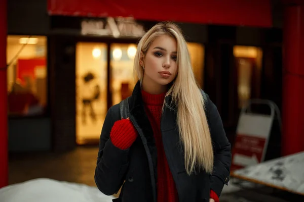 漂亮的年轻女子穿着时髦的大衣与袋子走近商店橱窗和购物 — 图库照片
