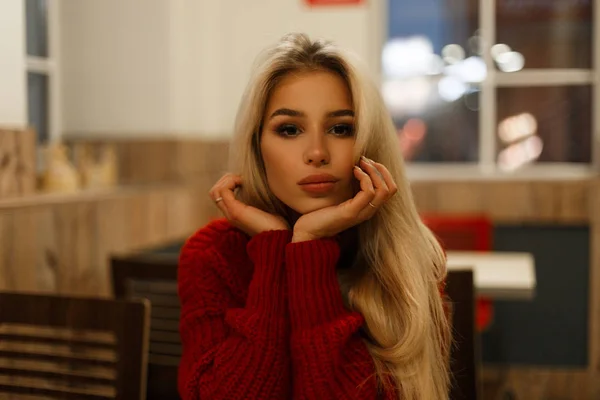 穿着时髦的红色毛衣的年轻美丽的妇女晚上坐在咖啡馆里 — 图库照片