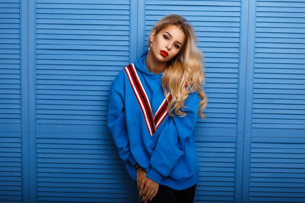 Snygg ung tjej i en mode hoodie nära en blå trävägg — Stockfoto
