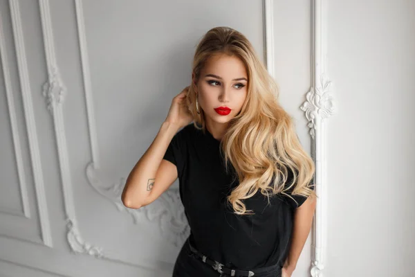 Belle jeune femme à la mode avec des lèvres rouges dans un débardeur noir près d'un mur élégant blanc — Photo