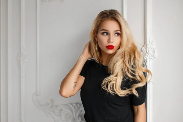 Elegante junge schöne Frau mit roten Lippen in einem schwarzen stylischen T-Shirt in der Nähe einer weißen Vintage-Wand — Stockfoto