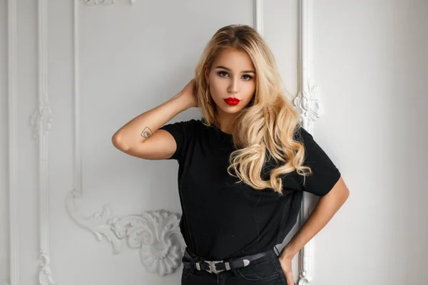 Elegante bella giovane donna in una moda nera T-shirt vicino a un muro bianco — Foto Stock