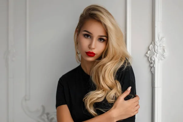 Modelo de mujer joven y elegante con un peinado con labios rojos en una camiseta negra de moda cerca de una pared blanca —  Fotos de Stock