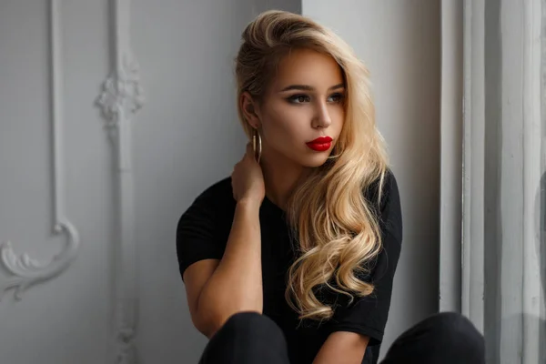 Belle jeune fille modèle élégant avec des lèvres rouges dans une chemise noire de mode assis près de la fenêtre — Photo