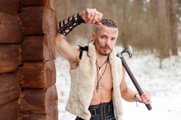 Viking com um machado em um colete de lã perto de uma casa de madeira na floresta — Fotografia de Stock