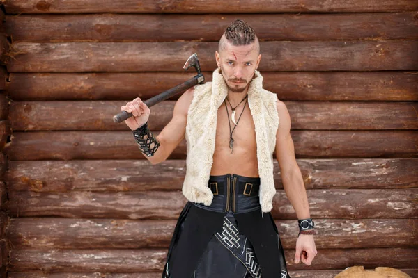 Guerreiro viking com um machado em um colete de uma pele perto de uma parede de madeira — Fotografia de Stock