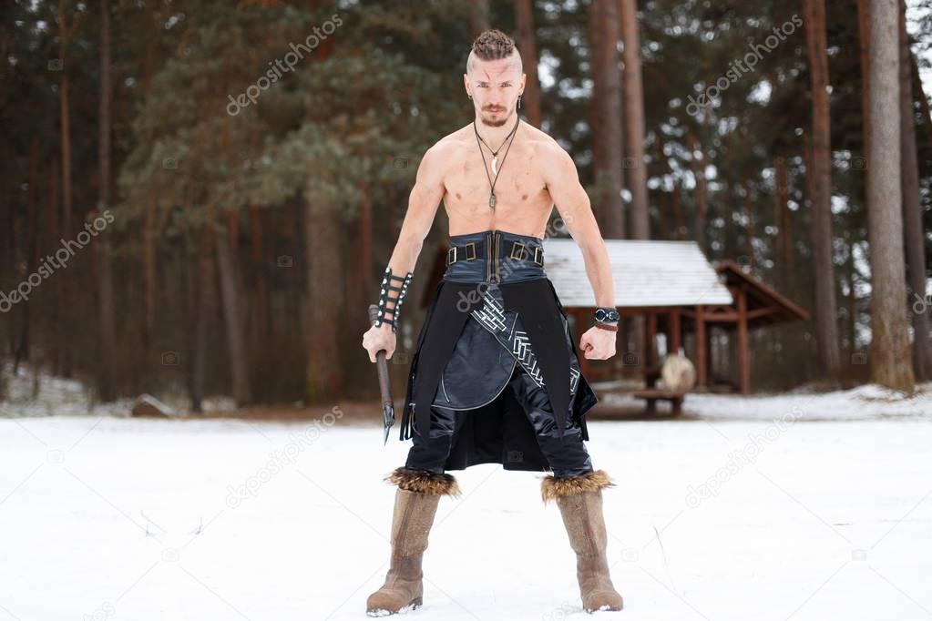 Viking man warrior with an ax in a leather skirt with boots with in the winter forest
