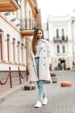 Örgü kazaklı, mavi kotlu, şık paltolu, spor ayakkabılı güzel bir kadın şehirde yolda yürüyor. Şirin kız model, sıcak bir sonbahar gününde sokaklarda gezer..