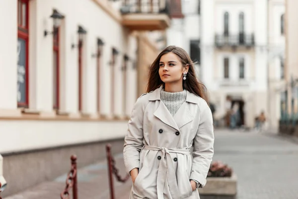 Pretty attractive elegant young woman in a vintage trench coat walks around the city near vintage buildings. Beautiful cute girl model on a walk on an autumn warm day. New collection female outwears. — 스톡 사진