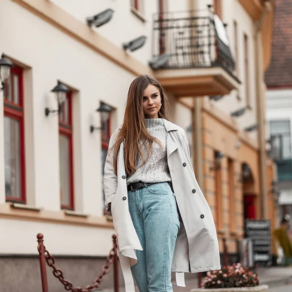 Pretty urban young woman with brown hair in elegant stylish trench coat walks outdoors in the city. Cute beautiful stylish girl fashion model poses outdoors. Fashionable seasonal women's outerwear. — Stockfoto