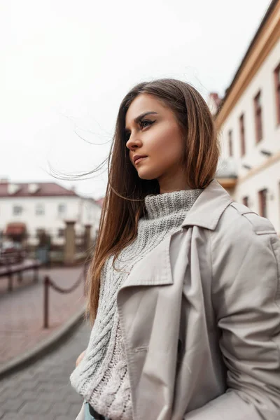 Europea modelo joven linda mujer en un suéter de punto de moda en un abrigo elegante disfruta de un descanso al aire libre en un cálido día de otoño. Hermosa chica urbana camina por la calle. Estilo juvenil casual . — Foto de Stock