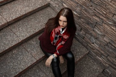Eski örülmüş bordo süveterli, siyah deri pantolonlu, taş bir merdivende oturan Avrupalı güzel bir kadın. Modayı takip eden kız model sokaklarda dinleniyor..