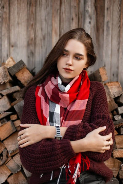 Piękne wiejskie młoda kobieta w stylowych dzianin ciepłe ubrania w vintage szalik pozowanie w pobliżu starej drewnianej stodole na zewnątrz miasta. Atrakcyjne słodkie dziewczyny model stoi w pobliżu ściany z drewna na opał. — Zdjęcie stockowe