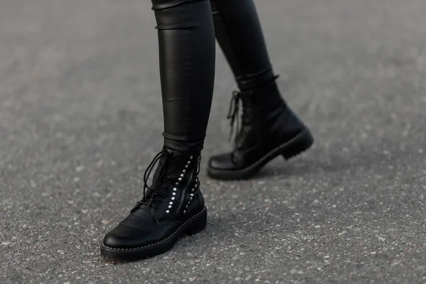 Gros plan des jambes féminines en bottes noires en cuir à la mode. Fille urbaine en legging élégant dans des chaussures à la mode marche sur l'asphalte dans la rue. Style d'automne décontracté . — Photo