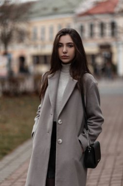 Güz gününde şehirde çantasıyla poz veren, şık bir golf sahasında kahverengi saçlı, şık bir kadın modeli. Modaya uygun bir kız sokakta dikiliyor. Bahar-sonbahar tarzı.