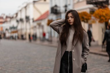 Zarif bir ceketle şık bir deri etekle şık siyah bir çanta taşıyan güzel bir genç kadın şehrin klasik bir sokağına bakıyor. Çekici kız bir sonbahar gününde dışarıda poz veriyor..