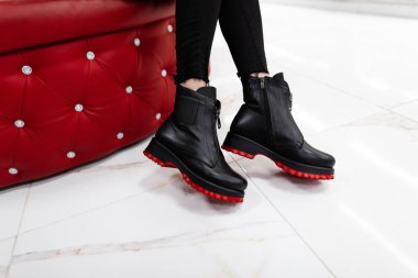 Mevsimlik kadın botları koleksiyonu. Parlak bir odada yumuşak bir sandalyede oturan kotlu kırmızı tabanlı, son moda bahar deri ayakkabılı şık genç bir kadın. Alışverişe. Yakın plan..