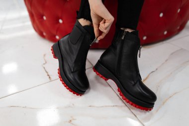 Modaya uygun bir kadın bir mağazada oturup sonbahar ayakkabılarını ölçer. Şık kotlu, kırmızı tabanlı siyah çizmeli kadın bacaklarının yakın çekimi. Yeni sezonluk kadın ayakkabıları koleksiyonu.