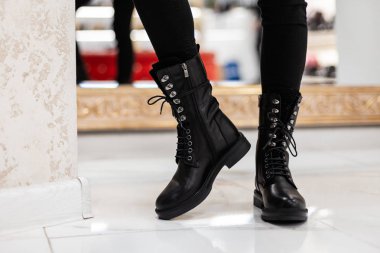 Aydınlık bir odada, deri, dantelli çizmeli kadın bacaklarını kapat. Eski kotlu şık bir kız bir mağazada şık ayakkabılar giyiyor. Gündelik sonbahar tarzı. Modaya uygun yeni koleksiyon.