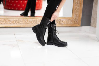 Genç bir kadın, bir alışveriş merkezinde aynanın yanında şık siyah kotlu, modaya uygun siyah deri çizmeli bir şekilde dikiliyor. Sonbahar-bahar moda kadın ayakkabıları koleksiyonu. Bacaklarını kapat..