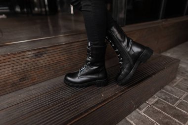 Siyah kotlu, deri, şık, dantelli çizmeli kadın bacaklarının yakın çekimi. Modaya uygun bir kadın kapalı alandaki ahşap merdivende duruyor. Retro tarzı. Sonbahar moda kadın ayakkabıları.