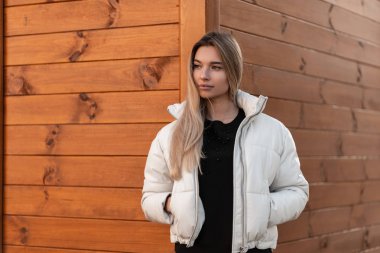 Sokakta, ahşap bir binanın yanında, şık beyaz ceketli, siyah süveterli, hoş, genç bir kadının portresi. Şehirde doğal makyajı olan modern güzel bir kız..