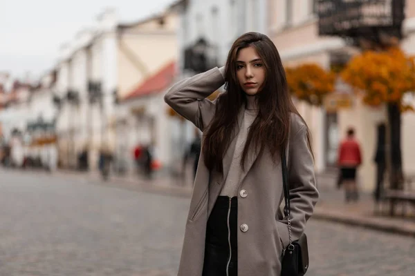 Mujer joven de moda en ropa de abrigo elegante con un bolso posando en una calle vintage en la ciudad en un día de otoño. Muchacha atractiva modelo al aire libre. Ropa de mujer de moda. Estilo otoño-primavera . — Foto de Stock