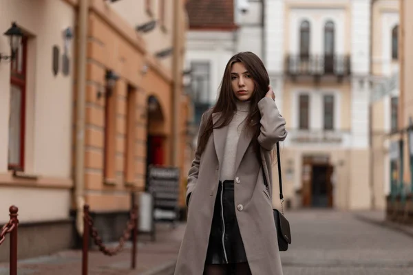 멋지고 아름다운 옷을 입은 젊은 여성 이 가죽 스타일의 검은 핸드백을 들고 시내 빈티지 건물 근처에 서 있습니다. 가을 날 야외에서 유럽 도시 소녀. 가을 스타일. — 스톡 사진