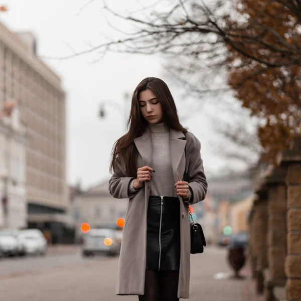 Modelo de uma jovem mulher bonita em outerwear elegante com um saco de couro preto posando ao ar livre na cidade. Modelo de moda menina bonito moderno gosta de andar na rua. Roupas de outono feminino na moda . — Fotografia de Stock