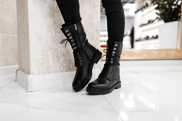 Young trendy woman in black stylish jeans in fashionable leather lace-up boots stands on the white tile in the mall. Fashion collection of women's autumn shoes. Close-up of female legs in footwear. — Stock Photo, Image