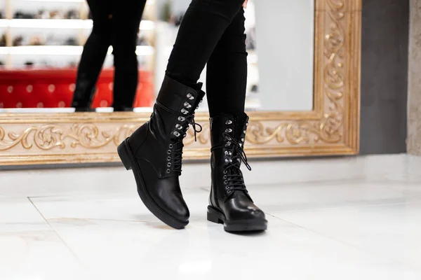 Detailní záběr ženských nohou v módních kožených černých botách na krajkách ve starých džínách uvnitř. Stylová dívka v módních botách stojí na dlaždici u zrcadla v obchodě. Nenucený styl podzim-jaro. — Stock fotografie