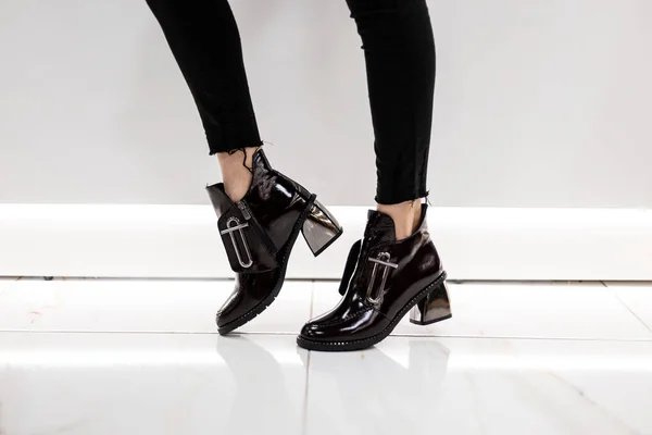 シルバーヒールでファッショナブルな特許ブラックブーツでヴィンテージジーンズの女性の足の閉鎖。女の子はショッピングセンターに立って、秋の靴を選択します。新しいコレクションの女性の季節の履物. — ストック写真