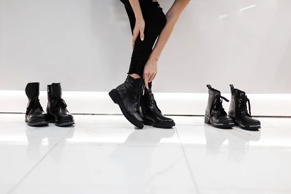 Mladá žena stojí v obchoďáku vedle bot ve stylových černých džínách a módních černých kožených sezónních černých botách. Podzimní a jarní módní kolekce dámské obuvi. Detailní záběr na nohy. — Stock fotografie