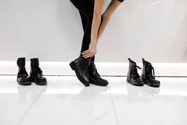 Женские ноги в модных кожаных черных осенних сапогах в стильных черных джинсах. Модная девушка стоит в магазине и измеряет обувь. Современная молодежная повседневная одежда. Детали повседневного вида. Крупный план . — стоковое фото