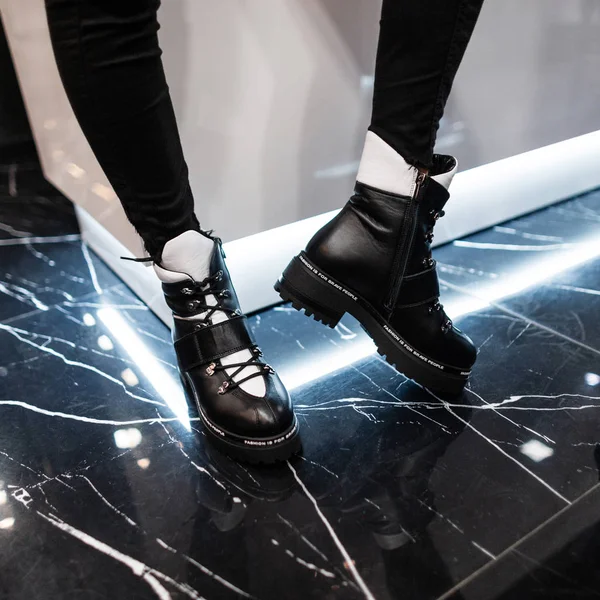 Közelkép női lábak divatos bőr fekete-fehér csizma egy modern szobában. Stílusos lány farmerben divatos cipőben áll egy boltban. Alkalmi őszi-téli stílus. Divatos új kollekció. — Stock Fotó