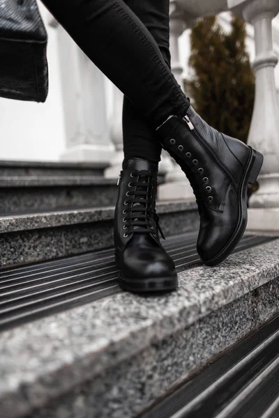 Сезонная коллекция женских сапог. Стильная молодая женщина в модных весенне-осенних черных кожаных кружевных туфлях в джинсах стоит на каменных ступеньках на улице. Крупный план . — стоковое фото