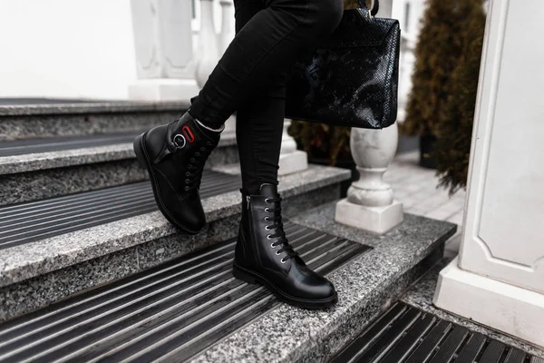 秋-冬の女性の靴のファッショナブルな新しいコレクション。ブラックスタイリッシュなブーツでヴィンテージジーンズの女性の足のクローズアップで流行の革のバッグ. — ストック写真