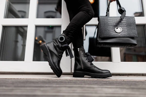 スタイリッシュな女性が靴を履いて通りに立っている。流行の革の黒のヴィンテージブーツでファッションハンドバッグとファッショナブルなジーンズの女性の足のクローズアップ。女性の履物の新しい季節のコレクション — ストック写真